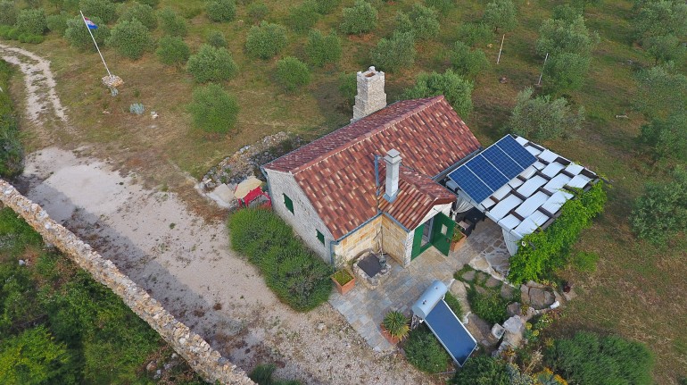 Aerial view on the house. The fluepipe, the solar panels, the water-pump, the tank, the gazebo and the olive trees are visible.