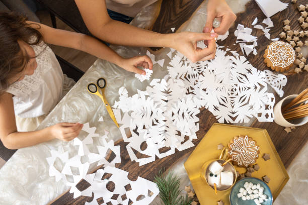 Mom and daughter make Christmas decorations with paper cutting in the form of snowflakes.