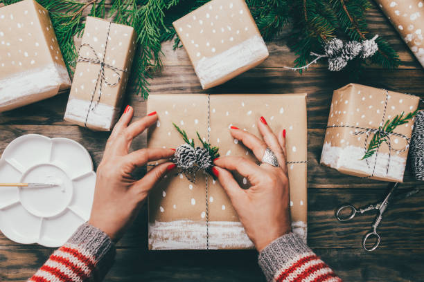 Woman’s hands pack Christmas gifts on brown paper decorated with painted snow,