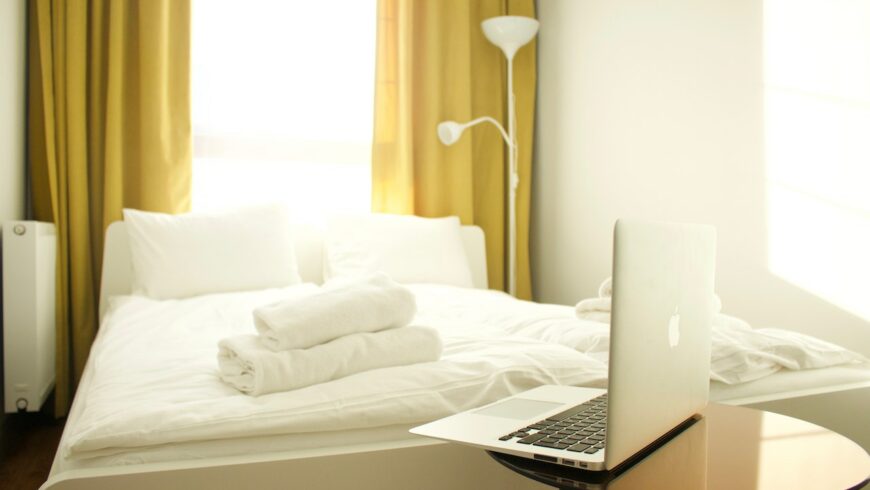 A bed with white sheets and towels; a laptop on a table