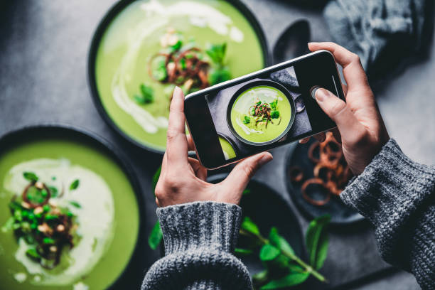 healthy eating blog: a woman taking a photo of green cream soup with her mobile phone. 
