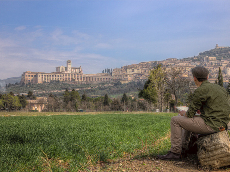 the city of Assisi on the top of an hill seen by a painter sitting at the foot of the hill