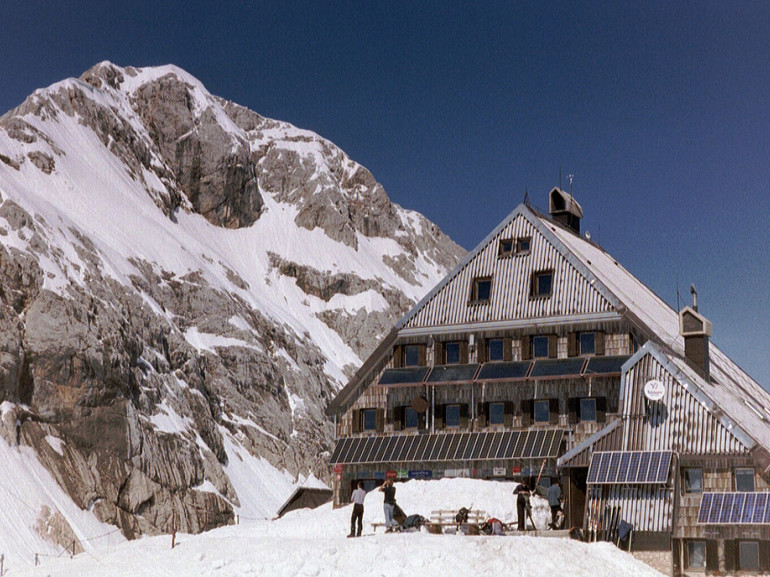 A mountan hut surrounded by snow at the foot of a mountain