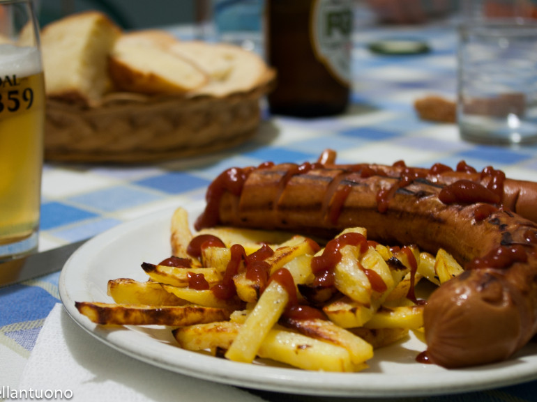 a plate with sausages and french fries on the table with a glass of beer